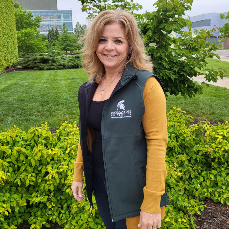 Person wearing a green zippered vest with white embroidered College of Osteopathic Medicine logo on the left upper chest. 