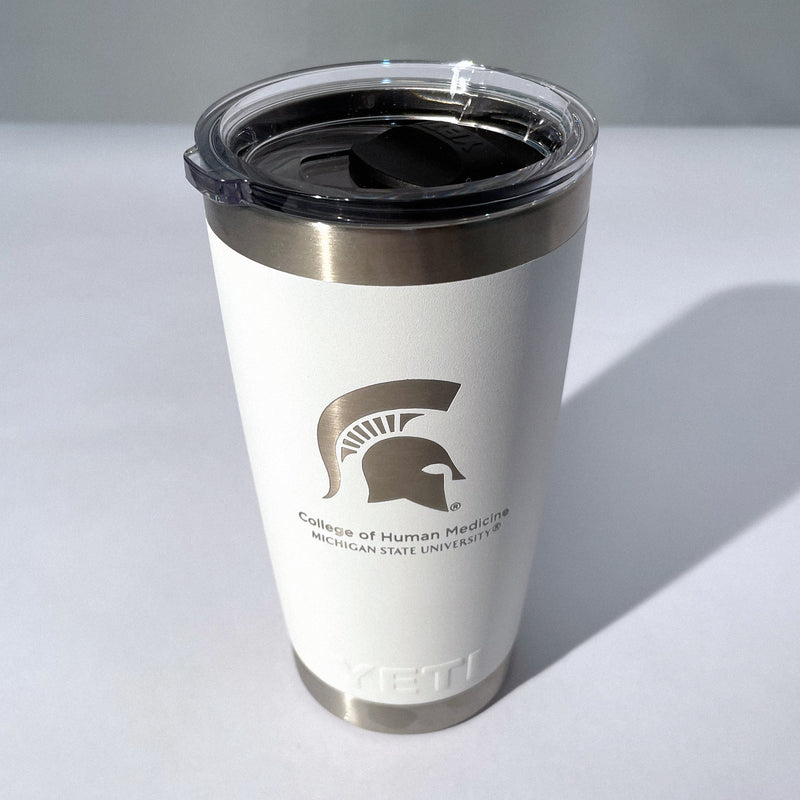 A white, 20-ounce beverage tumbler with a silver etched logo that includes a picture of the spartan helmet and the words Michigan State University College of Human Medicine. This top-down angle shows off the clear lid