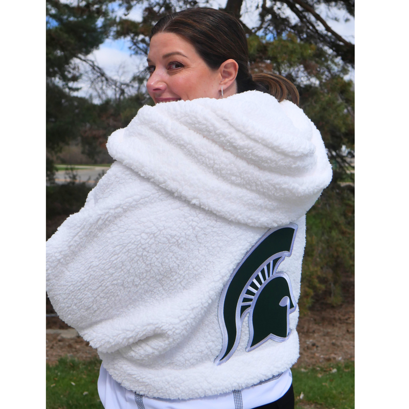 Back of person wearing white sherpa with hood with large green Spartan helmet patch on the center. Hits at waist. 