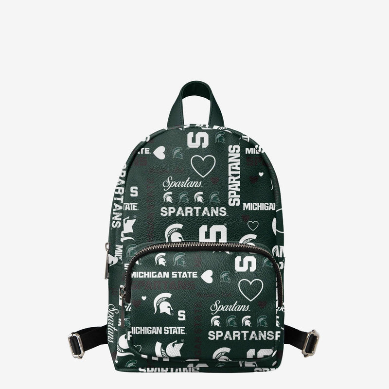 Front view of the forest green mini backpack with various Michigan State logos and heart icons in white and black. The top handle is solid green while the back straps are black.