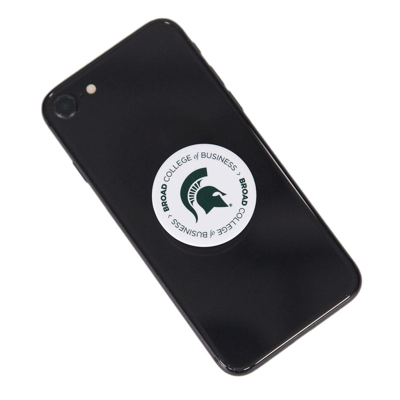 Back of a black cell phone with a white circular pop socket affixed in the center. On the pop socket, text reads Broad College of Business (with Broad in bold) twice in a circle around a forest green Spartan helmet.