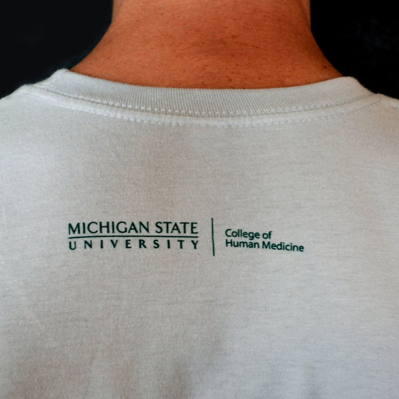 Close-up of the College of Human Medicine wordmark logo, printed in green just underneath the neckline on the back of the t-shirt