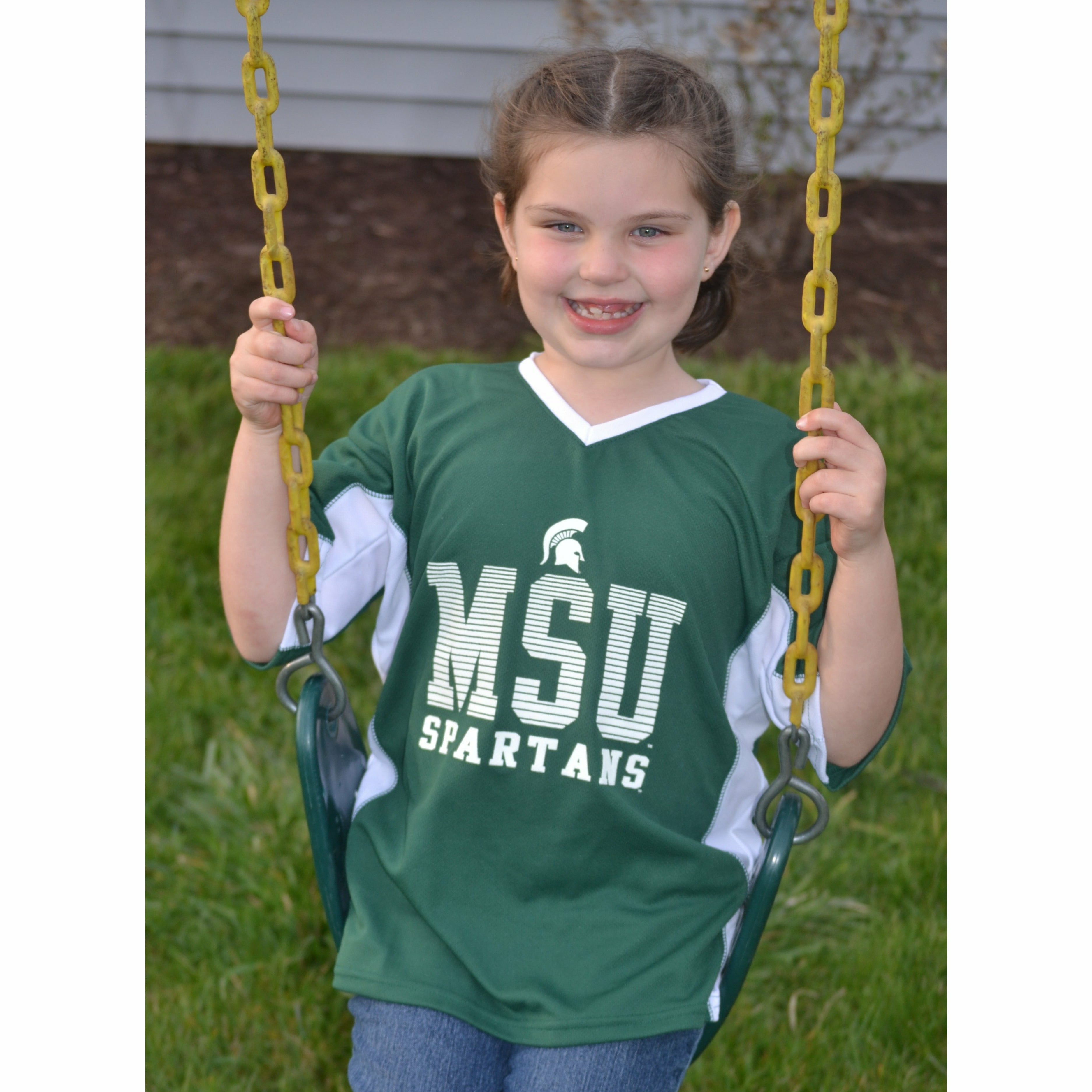 A young girl sits on a swing wearing the Youth Athletic T-shirt over jeans