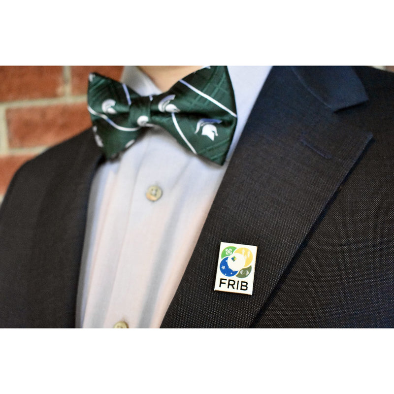 Close-up of a navy suit with the FRIB pin attached to the lapel. The wearer has a green bowtie featuring white Spartan helmets on as well.