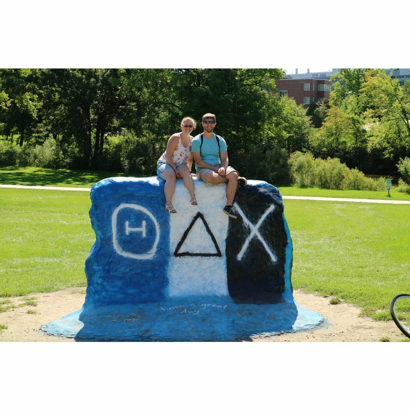 The rock painted with greek letters and blue, white, and black stripes. Two of the designated guardians sit atop the rock.
