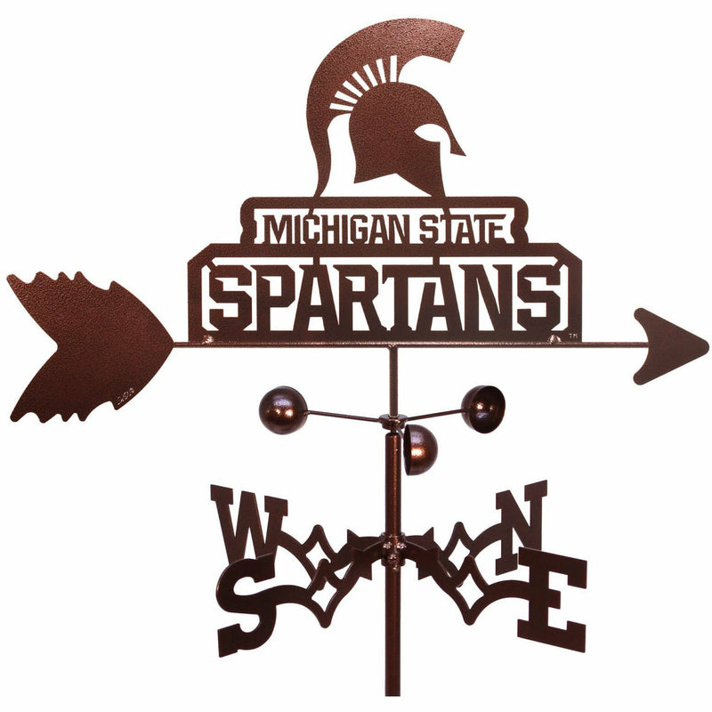 Close-up of the copper weathervane's top, which above the arrow has a Spartan helmet over text reading Michigan State Spartans. Below the arrow is a three-pronged spinner, which is above four-directional extension with letters indicating North, East, South, and West, respectively.