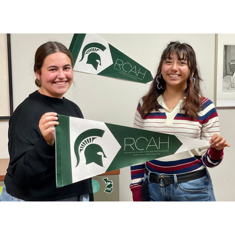 Two students hold up the RCAH pennant in Snyder Phillips hall, where the RCAH pennant is also hung on the wall behind them.