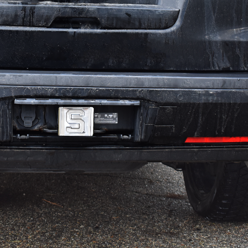 The chrome Spartan block S hitch cover in use on the back of a black SUV