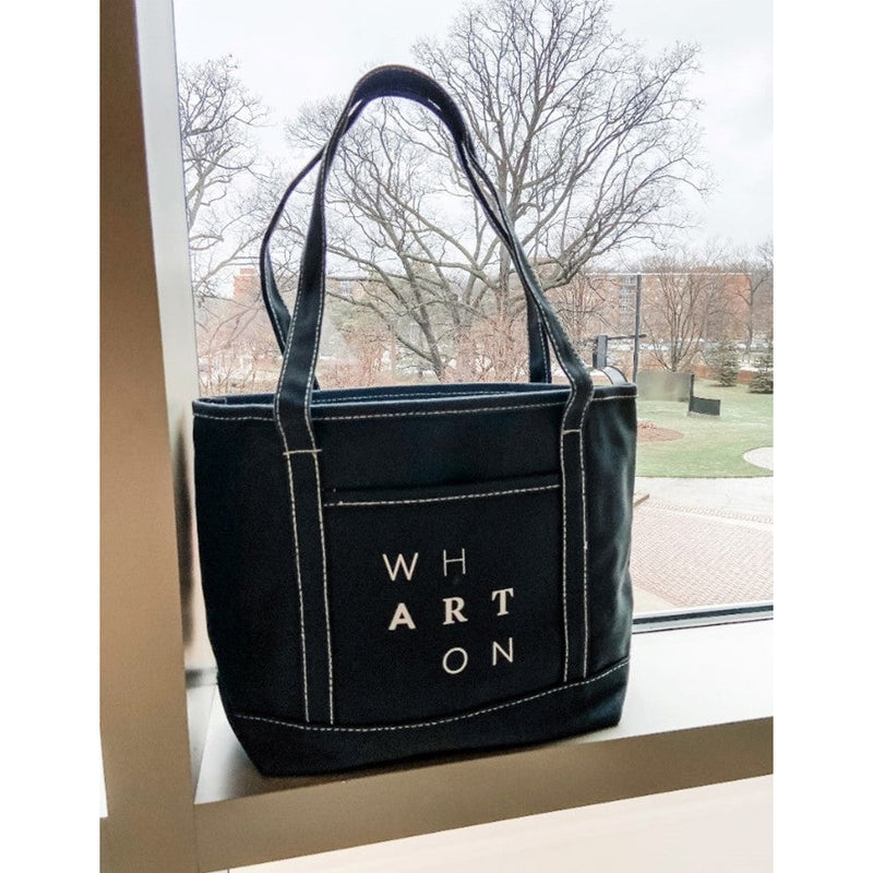 A black cotton and canvas tote bag. On the side of the bag spells the word Wharton in a staggered formation.