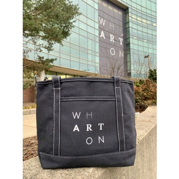 A black cotton and canvas tote bag. On the side of the bag spells the word Wharton in a staggered formation. 